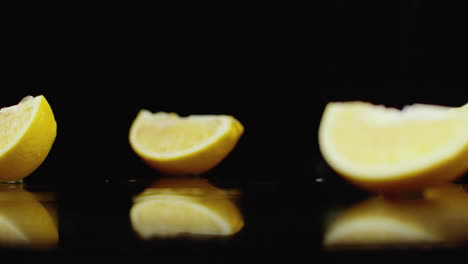 Eine-Saftig-Geschnittene-Gelbe-Zitrone-Fällt-Auf-Ein-Glas-Mit-Wasserspritzern-In-Zeitlupe-Auf-Dunklem-Hintergrund
